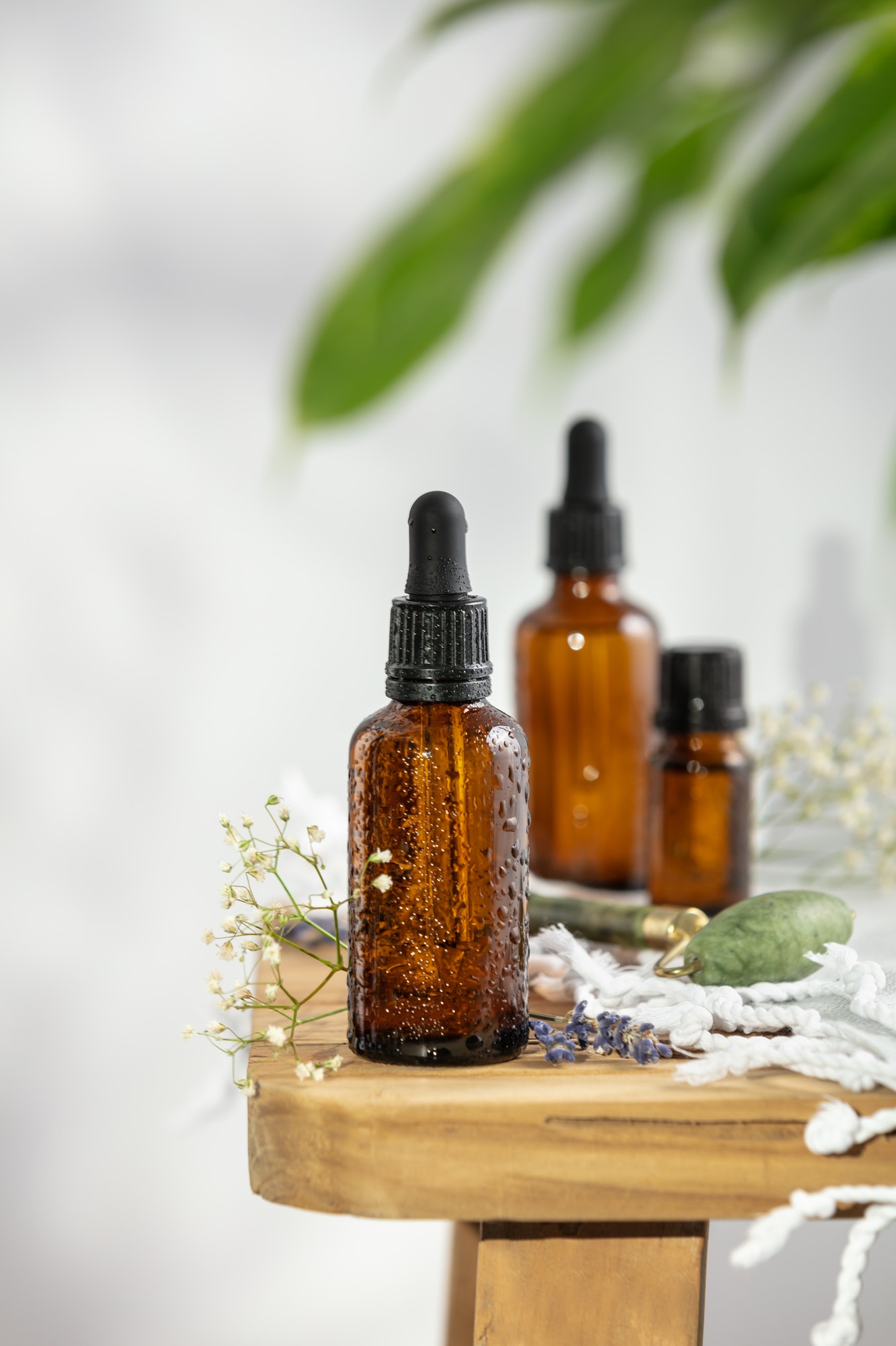 Bottles of dark amber glass with essential oil, massage jade roller and tropical leaves